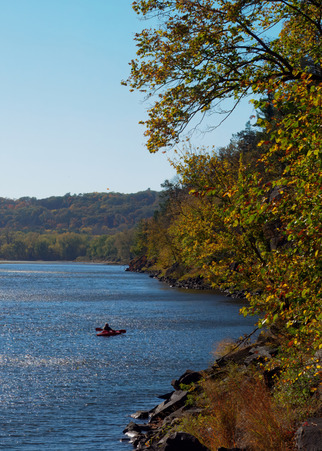 A person kayaks along a calm river in fall. 