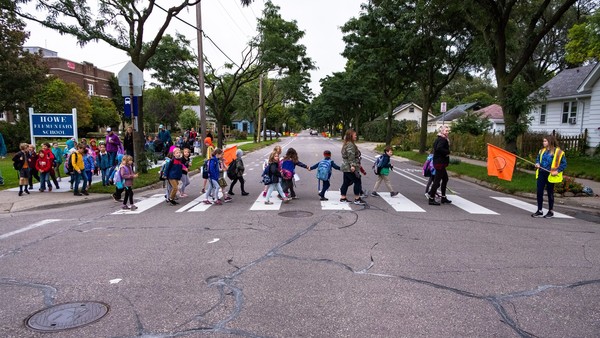 Large group of children crossing the street with crossing guards.
