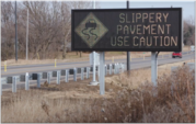 Roadway sign with message "slippery pavement, use caution".