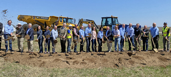 People stand in a line in front of heavy equipment and use gold-painted shovels to break ground at the Hwy 23 Groundbreaking.
