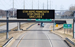 A near-empty highway with a message sign reading "Stay home Minnesotan. Stop COVID-19. Save lives."