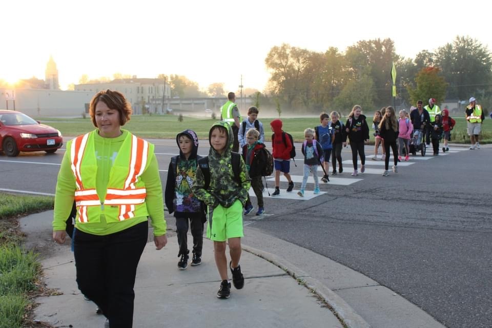 Crossing guards and a long line of kids are walking to school. The group is walking while css