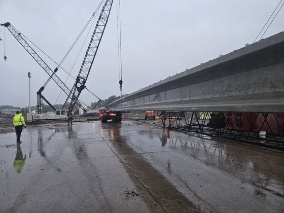 Bridge beam at Fourth Street Northwest is prepared to be set over Interstate 90 in Austin on a rainy day with bridge inspector watching.