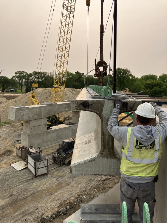 Bridge beam is moving into place with construction worker guiding it.