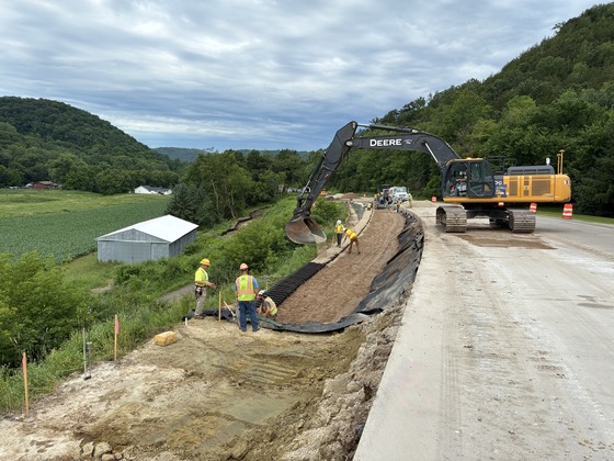 Photo showing construction workers and an excavator that is filling geocells along Highway 14 on Stockton Hill.