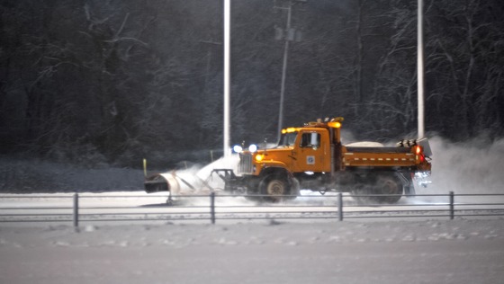 An orange MnDOT snow plow removes snow from a road.