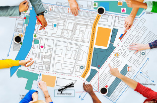 Eight hands populate the perimeter of a development plan, some hold markers, some point at design features, some are at rest.