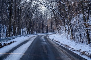 Streams of dappled sunlight fall across a roadway partially covered in snow and ice.