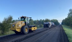 Large equipment pours and compacts fresh asphalt onto a road