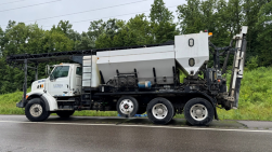 A low slump overlay truck is seen in profile while parked on the side of the road.