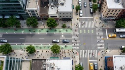 A bird's eye view of a vibrant streetscape intersection with pedestrians, cyclists, buses, motorists, and complete streets design elements
