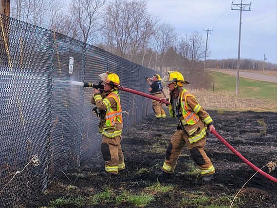 Firefighters point a hose at a smoking field