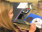 Woman sitting at a table and painting a dog on a canvas