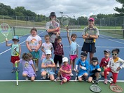 Group of kids and tennis instructors posing for a photo on the tennis court