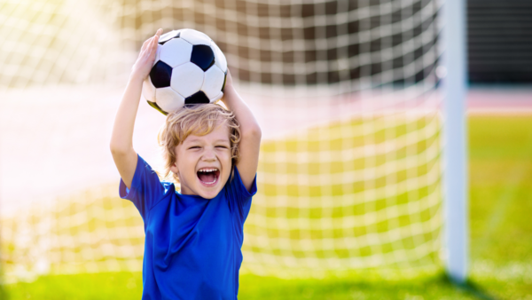 Young boy holding a soccer ball in front of a goal