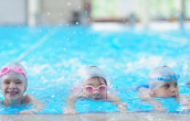 Three kids wearing swim goggles in a pool 