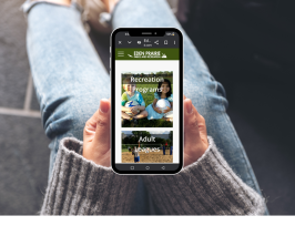 Hands holding a mobile phone that's displaying the Eden Prairie Parks and Recreation registration page