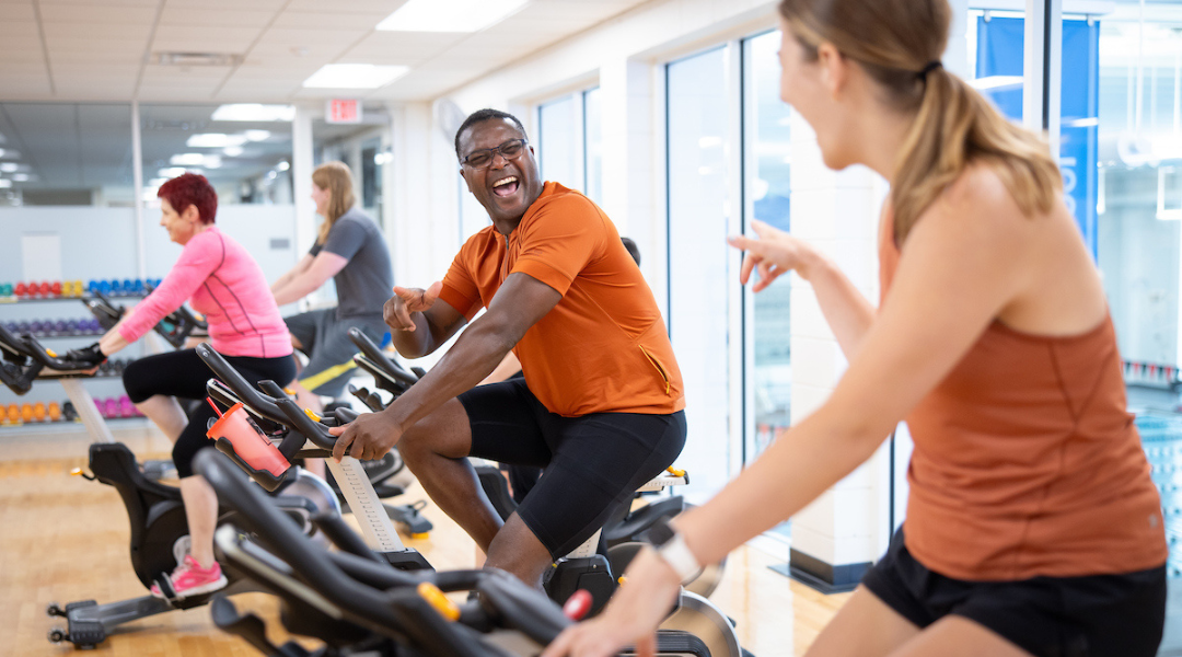 two Community Center members smiling and pointing at each other during a cycling class