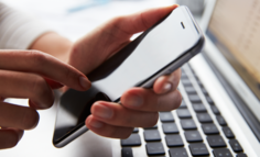 Hands using a cell phone near a laptop