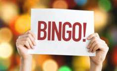 Hands holding up a sign that says Bingo! in front of blurred colorful lights