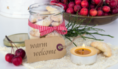 Note that says "Warm Welcome" surrounded by cranberries, jar of biscuits and candle