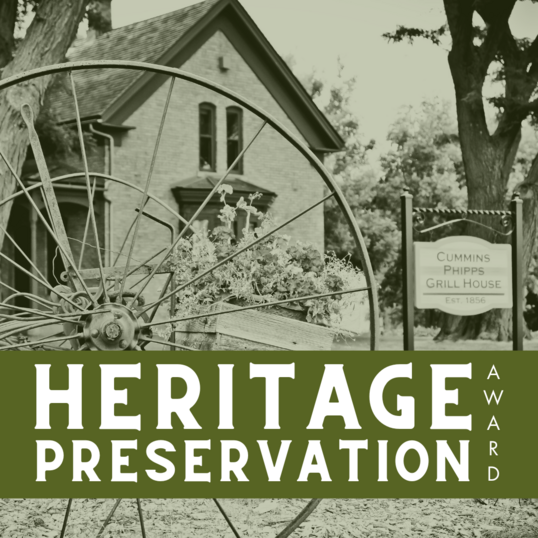 "Heritage Preservation Award" with background of old wagon wheel in front of a historic building.