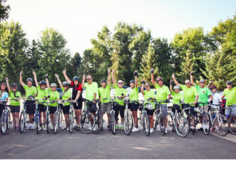 Long line of bicyclists wearing matching green t-shirts waving at the camera