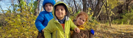 Three kids dressed in fall jackets and playing outdoors