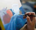 Close-up of a hand holding a brush to a painted canvas