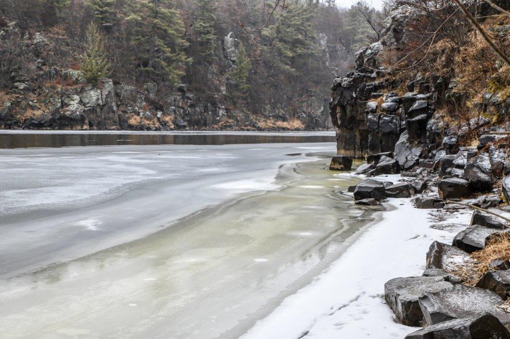 Frozen water along the river and rocky cliffs in winter
