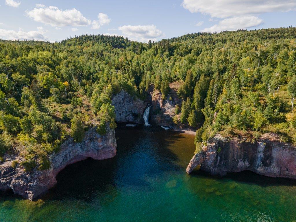 A stunning aerial view of Manitou River waterfall cascading into Lake Superior along Minnesota’s North Shore. Summer