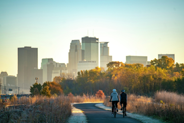 Two bicyclists on trail with Minneapolis skyline in background