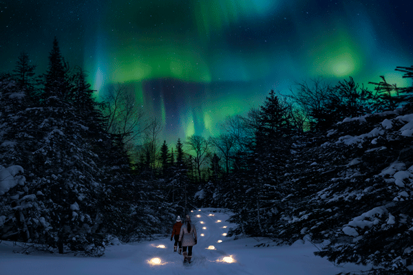 an image of people walking on a luminary-lit trail under the Northern Lights/Ryan Taylor