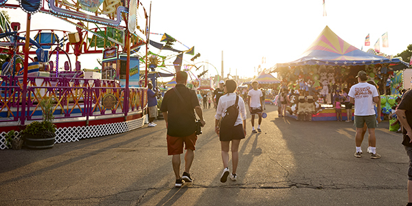Two people walking towards the sun while in the colorful Midway of the Minnesota State Fair