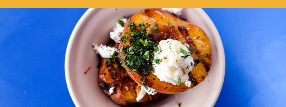 deliciously yellow-orange grilled peaches in a white bowl on a blue surface.