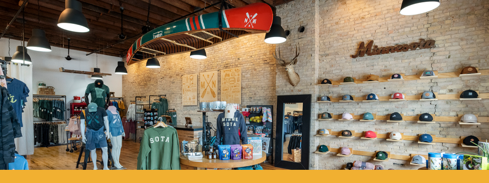 A white brick wall of flatback hats below a green and red canoe hanging from the ceiling, mannequins with SOTA apparel are throughout the floor
