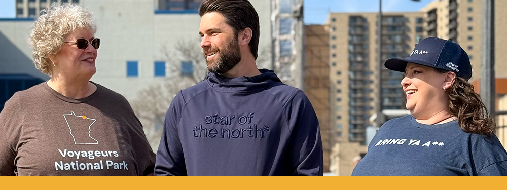 three friends casually talk downtown in various navy and brown Minnesota-themed shirts.