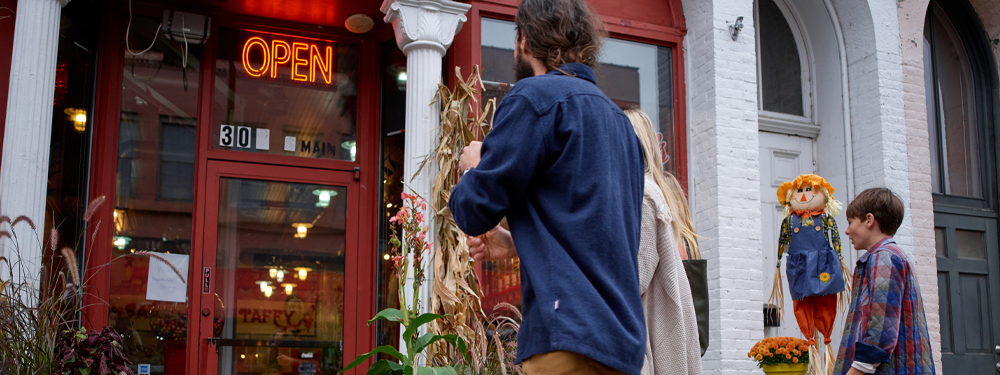 the backs of a family of four as they stride into a red candy shop with a neon orange "OPEN" sign.