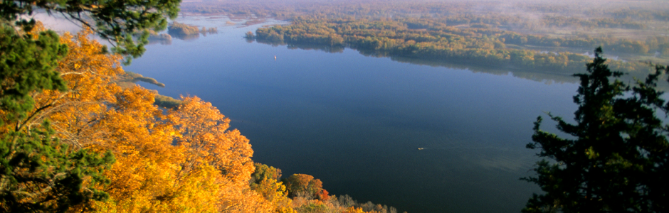 golden trees on a bluff tower over deep blue river waters