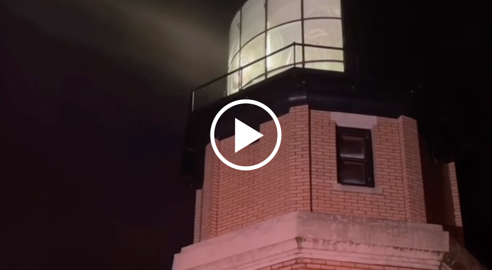 Video still: Split Rock Lighthouse with it's beacon lit, light beaming out in complete darkness