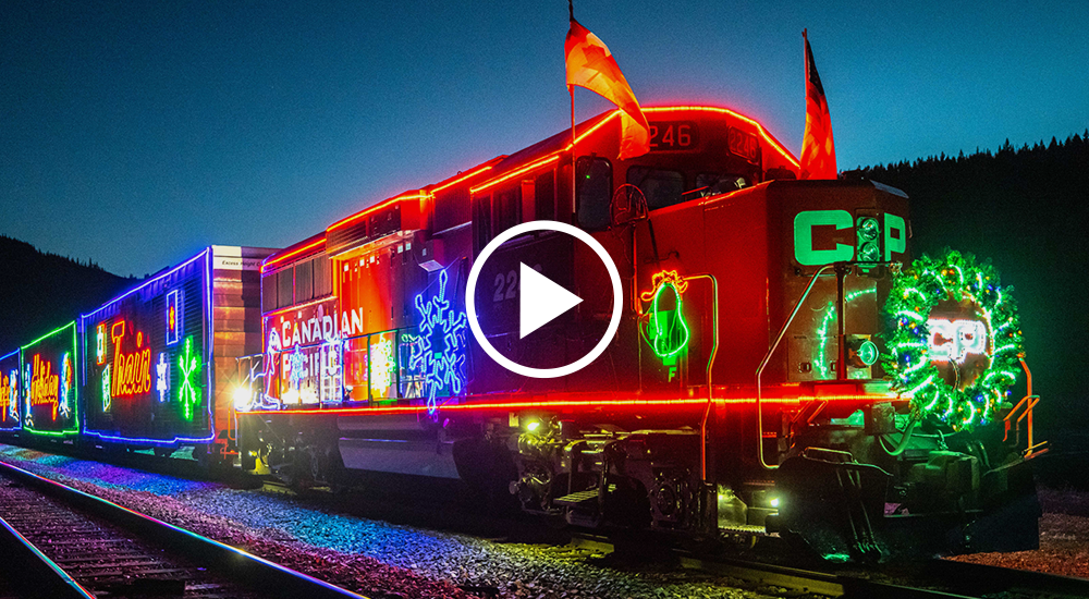 A Canadian Pacific train is decorated it moving and colorful lights. Snowflakes, wreaths, and bells are amongst the lighted subjects.
