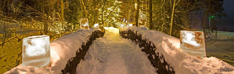 a stone bridge covered in snow and lit with ice luminaries provides a warm yellow glow along the path