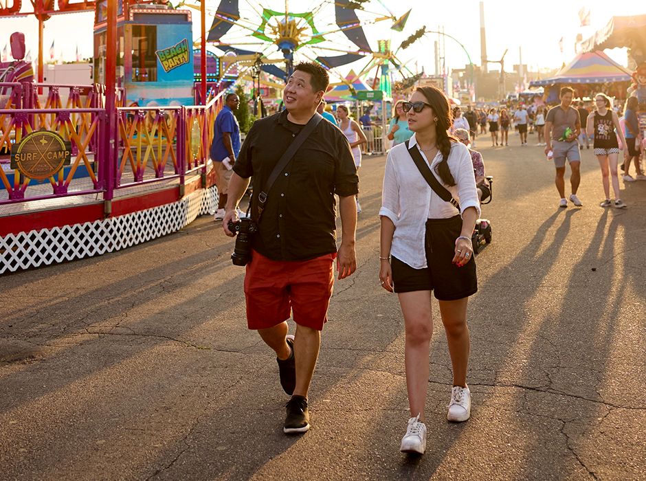 two people with cross-body bags look up as they walk through the midway rides at the Minnesota State Fair