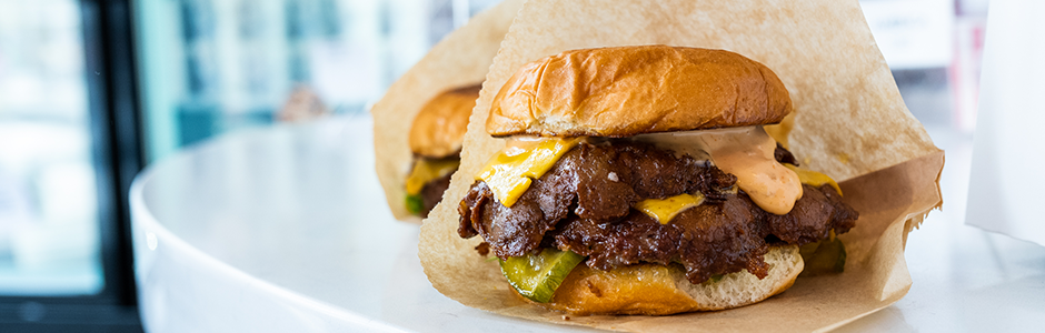 Side view of a double smash burger with gooey cheese and crunchy pickles, wrapped in brown paper.