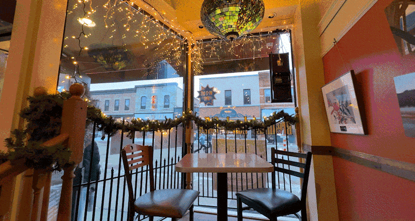 gif: garland and twinkle lights hang in the frosted window of a cozy cafe at dusk. a person opens the cafe door as two kids run down main street.