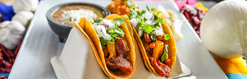 two hardshell tacos filled with meat and onion rest on a white plate.