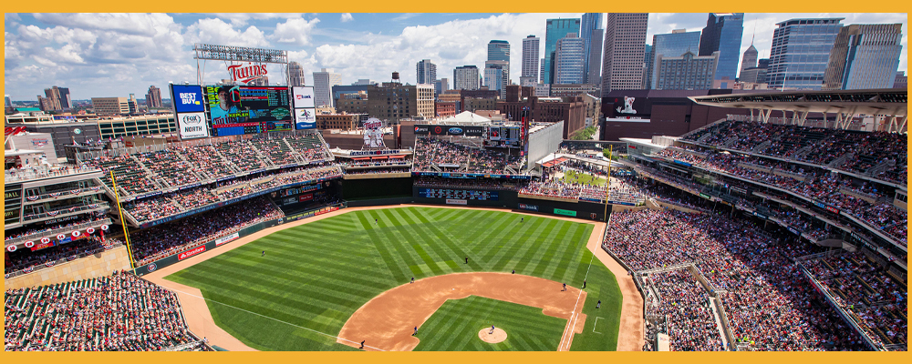 The Minneapolis skyline can be seen beyond the Target Field baseball field and stadium filled with people on a sunny day.