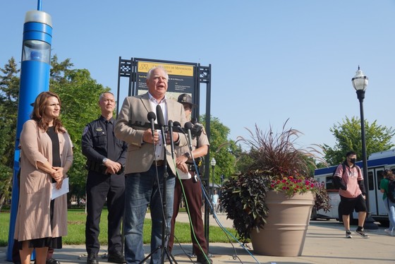 Governor Walz speaks in front of sign by state troopers and Lt. Governor Flanagan 