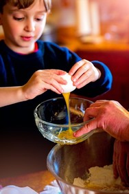 Photo of child cracking a raw egg into a bowl while cooking