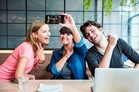 Photo of three people holding up a cell phone for a group selfie